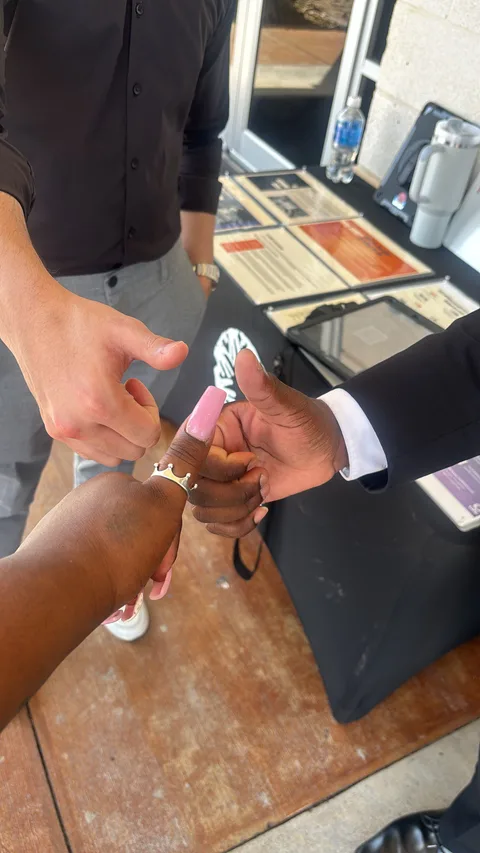 Three hands meeting in a thumbs-up beside a fundraising table